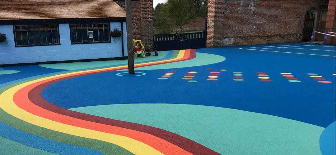 Colourful wet pour playground surfacing with rainbow pathway and activity markings installed in a school play area.